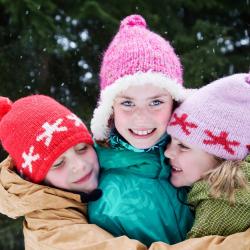 three kids hugging in front of evergreen trees