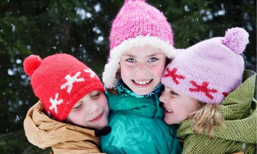 three kids hugging in front of evergreen trees